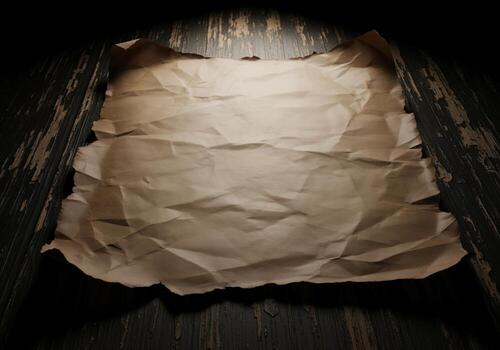 Aged crumpled parchment paper with torn edges resting on a dark distressed wooden surface photo