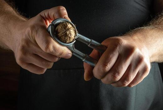 Hands skillfully use a metal nutcracker to break open a walnut, revealing the rich, textured shell and inner nut. The warm ambiance adds a touch of tradition and craftsmanship to the moment. photo