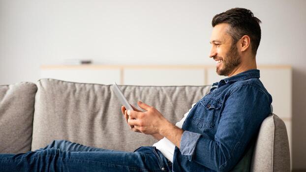 contento de edad mediana hombre en casual descansando en sofá a hogar, utilizando moderno teléfono inteligente, Copiar espacio. hermoso barbado hombre leyendo Blog o jugando juegos en el más nuevo móvil teléfono, lado ver foto