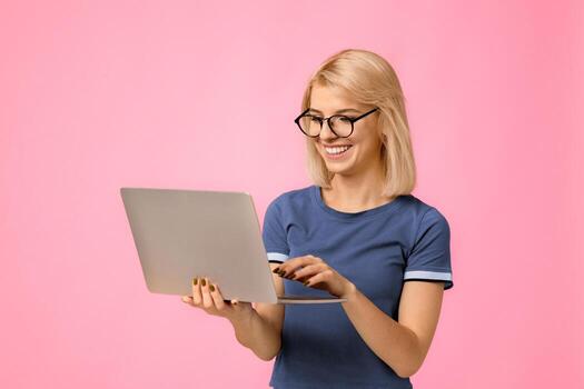 Work opportunities online. Happy lady with laptop computer in hands, surfing internet over beige background with empty space, studio shot. Woman standing with pc and looking at screen photo