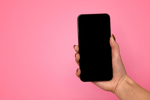 Technology concept. Female hand holding smartphone with black blank screen for mockup on yellow studio background with free space, browsing information or social media, using application, top view photo