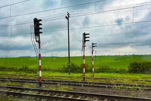 Railway signals and train tracks in the countryside on a cloudy rainy day. Transportation infrastructure with semaphore lights and green fields in the background photo