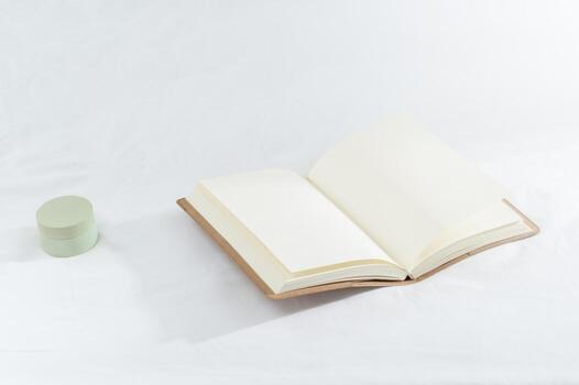 Open Notebook Resting on a White Surface With a Small Green Container Beside It photo