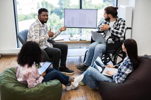 Diverse group of colleagues brainstorming together on architectural project using laptops and plans. Inclusive workplace featuring individuals of different races, genders, and abilities contributing photo