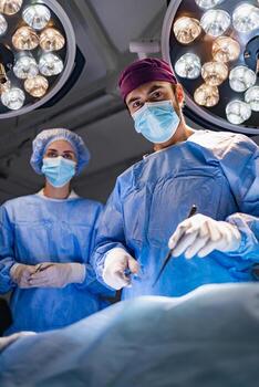 A surgeon and assistant are in an operating room, performing a procedure under bright lights. photo