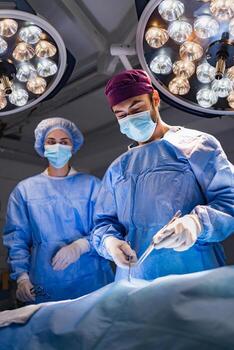 A surgeon and assistant perform a procedure in a modern operating room, illuminated by bright surgical lights. photo