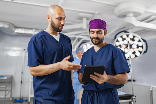 Two surgeons in scrubs discuss a patient's medical information in an operating room, using a tablet for reference. photo