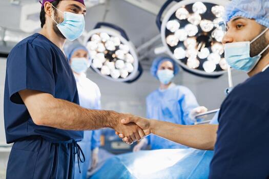 Two surgeons shake hands in an operating room, likely before or after a procedure, with medical staff and equipment in the background. photo