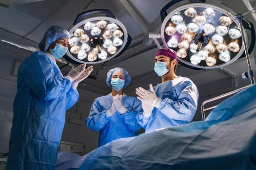 A surgical team in an operating room prepares for a procedure, illuminated by bright overhead lights. photo