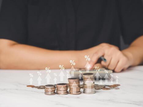 Close-up of coins stacked with percent symbol and arrows up and man using a calculator while sitting at the table photo