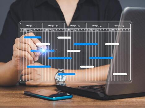 Project manager working on a laptop and updating tasks and milestones progress planning with a Gantt chart scheduling interface on a virtual screen. photo