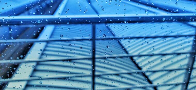 Raindrops streaking down a windowpane with a blurred balcony roof top in the background Pro Photo