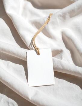 Blank white tag on soft white fabric with natural light photo