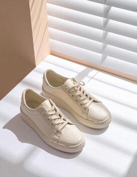 Elegant Beige Sneakers on White Surface with Shadow Play. photo
