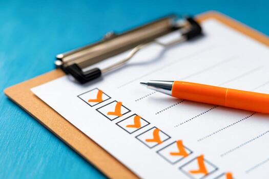 A checklist with orange check marks on a clipboard next to an orange pen resting on a blue wooden surface representing organization and task completion photo