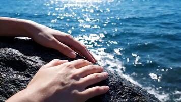 händer vilar på en riden kust sten med gnistrande hav i de bakgrund, skapande en video