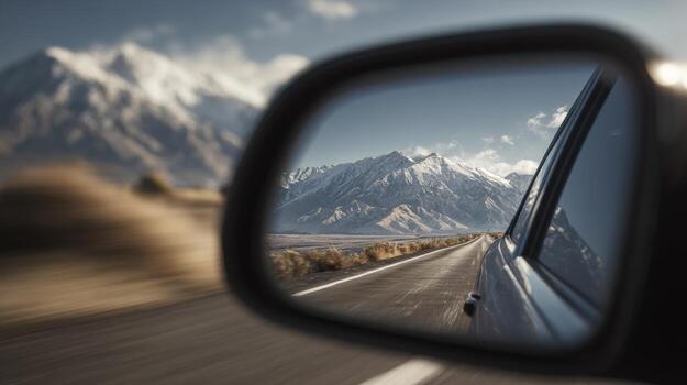 A breathtaking view of snow-capped mountains reflected in a car side mirror on a scenic road. photo