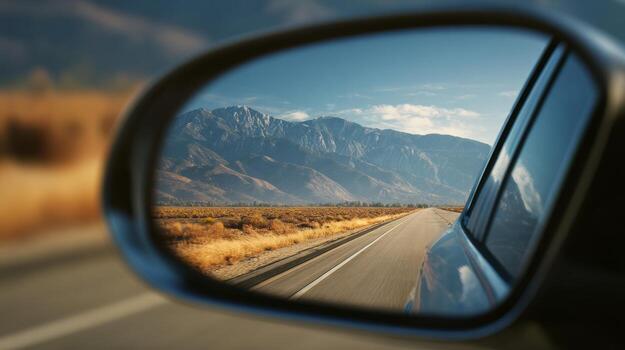 A stunning mountain view reflected in a car's side mirror, showcasing the open road and a clear blue sky. photo