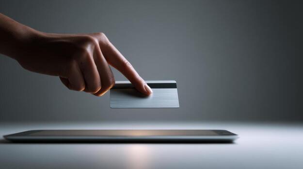 A close-up of a hand holding a credit card, poised above a tablet, symbolizing online shopping and digital transactions. photo