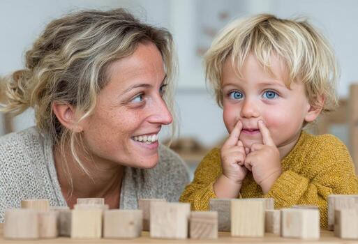 Smiling woman with curly hair interacts playfully with a young boy, showcasing a joyful moment of connection while surrounded by wooden blocks in a bright, inviting environment photo