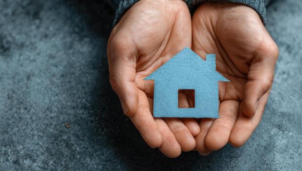 Hands holding a blue house-shaped object, symbolizing home ownership and real estate, with a textured gray background, conveying warmth and security in a personal space photo