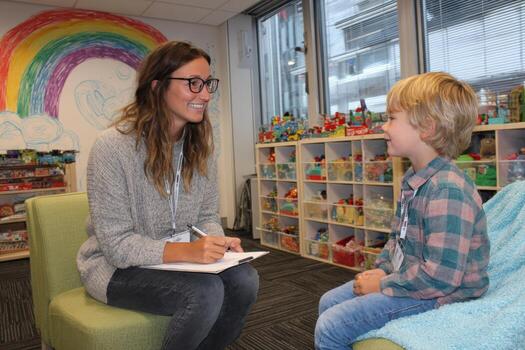 Female educator engaging with young boy in a colorful classroom setting, surrounded by toys and educational materials, fostering a positive learning environment photo
