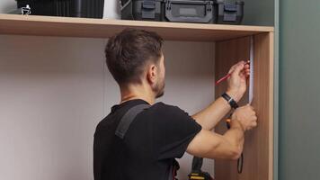 homem medindo de madeira gabinete, usando medindo fita e lápis para marca painel durante casa mobília montagem video
