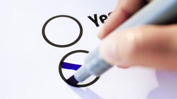 rösta, hand använder sig av en blå markör till dra ett x i de Nej cirkel på en frågeformulär, representerar avslag, oenighet, eller negativ beslut, närbild video