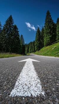 Scenic mountain road with a white arrow pointing forward through lush green trees under a blue sky photo