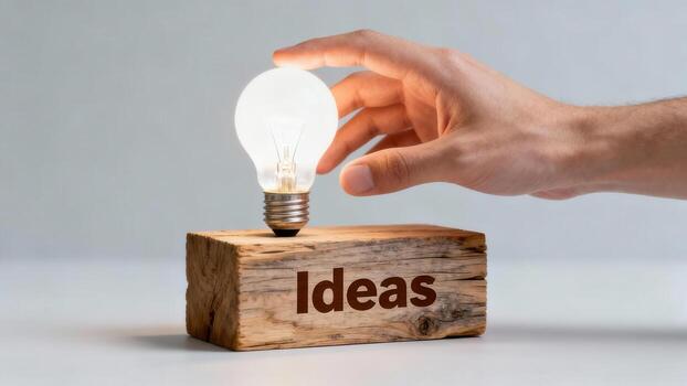 A hand reaches for a glowing light bulb resting atop a wooden block, symbolizing new ideas and innovation. photo