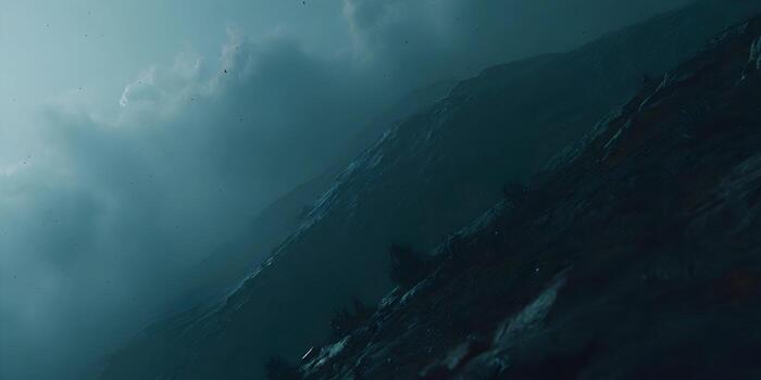 A dramatic view of a dark rocky mountainside under a cloudy moody teal sky with tiny particles floating in the air photo