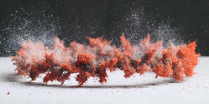 Red and white powder explodes upwards against a dark background creating a dynamic abstract visual photo
