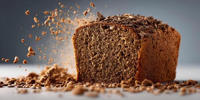 A whole wheat loaf of bread is exploding with scattered seeds and crumbs on a light surface photo
