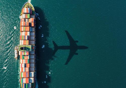 Massive cargo ship navigates vast ocean waters casting a striking airplane shadow, symbolizing global transport and logistics. photo