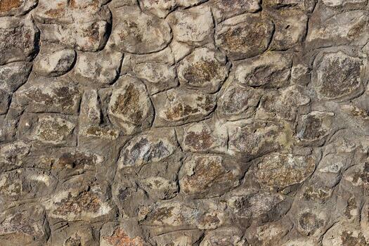 Old stone wall with irregular natural rocks set in mortar. Weathered textures, earthy tones, rough patterns, ideal for background, design element in architectural, historical, rustic-themed designs photo