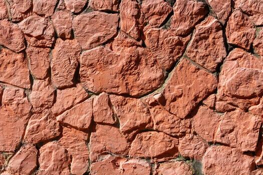 Close up of red stone wall with irregular rock pattern and visible mortar. Rough textured masonry surface suitable for backgrounds, construction, architectural design. photo