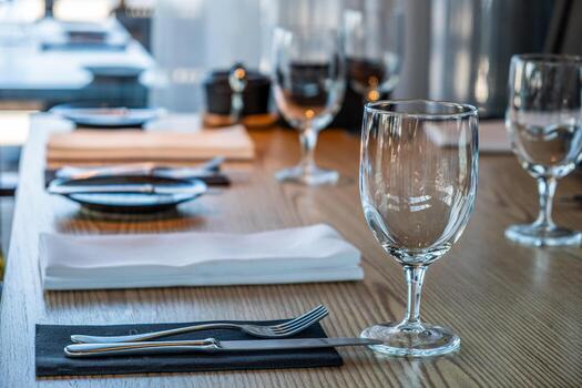 Elegant dining table setting with glassware, cutlery, and napkins arranged neatly on wooden surface, creating a sophisticated atmosphere for a culinary experience photo