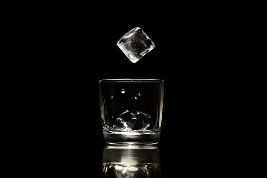 Ice Cube Falling into Glass of Water on Black Background photo