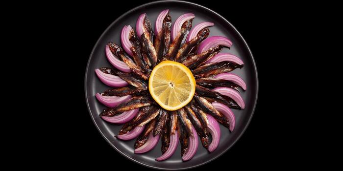 Overhead shot of a plate of sardines with red onion and lemon on black background photo
