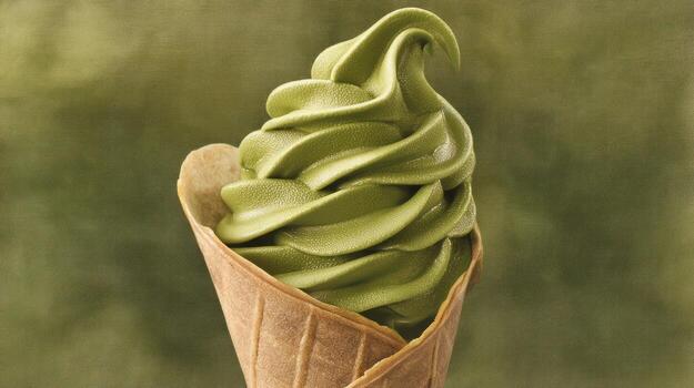 Swirl of green soft serve ice cream in a waffle cone against a blurred background photo