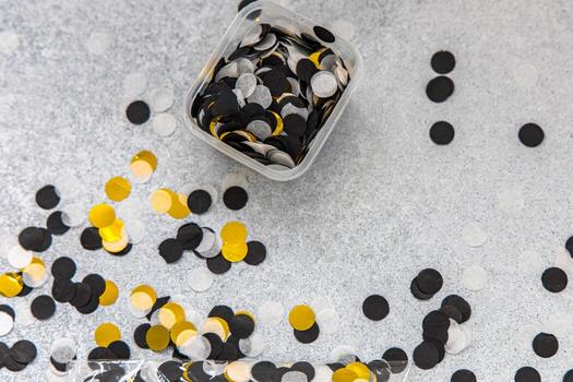 Colorful confetti scattered on a gray surface with an additional container of mixed shapes photo