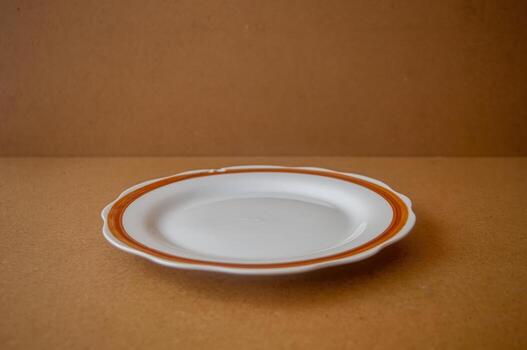 White ceramic plate with orange rim placed on brown surface highlighting minimalist tableware design, warm tones, and clean presentation for food styling or product display. photo
