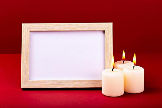 Mockup. Elegant wooden frame featuring blank with copy space is positioned next to three lit candles, creating warm and inviting atmosphere against vibrant red backdrop photo