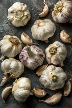 Various garlic cloves and bulbs are spread across a dark table, showcasing their unique shapes and rich textures in an inviting layout photo