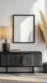 A small poster frame rests on a sideboard next to a lamp, surrounded by decorative elements in a serene, minimalist living area photo