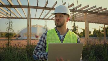 Thoughtful Caucasian male man experienced worker inspector helmet hardhat guy engineer technician typing laptop computer entering data internet pc analyzing project working blueprint construction park video