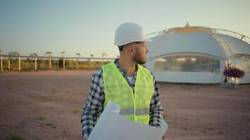 fundersam omtänksam professionell caucasian manlig man kille enhetlig ingenjör arbetstagare analyserar läsning projekt plan strukturera bygga planen förvirrad inspektör arkitekt ser runt om jordbruksmark fält parkera video