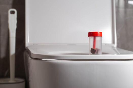 Sterile container with stool test on the toilet bowl in the toilet. Concept of stool testing for calprotectin and occult blood. Copy space for text photo
