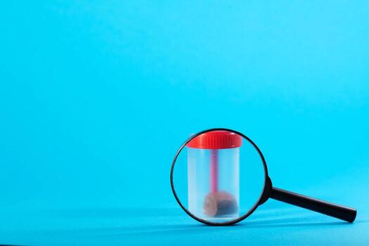Magnifying glass with stool analysis container on a blue background. Concept of stool tests calprotectin and protozoan parasites. Copy space for text, cologram photo