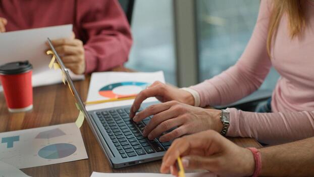 Three unrecognizable colleagues typing laptop paperwork unknown group business team informal workers using computer businesswoman cooperating with two businessmen analyzing documents circle diagram photo